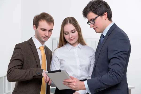 Dois homens de negócios com uma mulher entre olhar para o tablet. Conceito de trabalho em equipe . — Fotografia de Stock