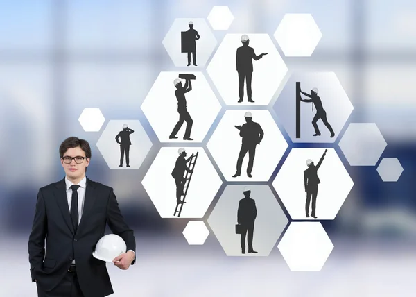 Businessman with white helmet, silhouettes of businessmen with different construction tasks in hexagonals near him, Blurred office background. Concept of business construction. — Stock Photo, Image