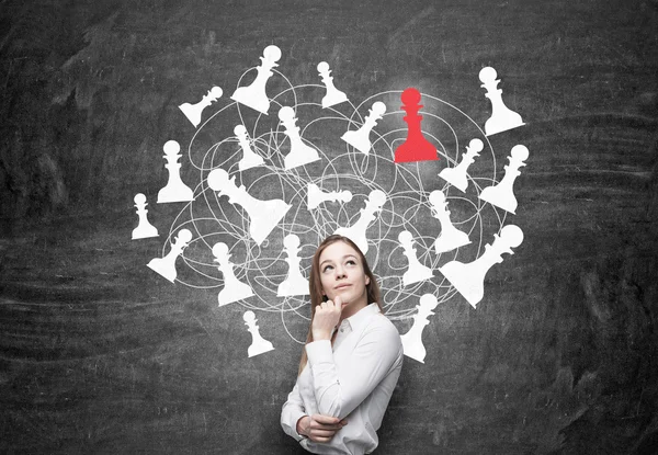 Бізнес-леді з рукою на підборідді, шахові фігури, намальовані на чорній стіні позаду, червоний пішак. Концепція гри . — стокове фото