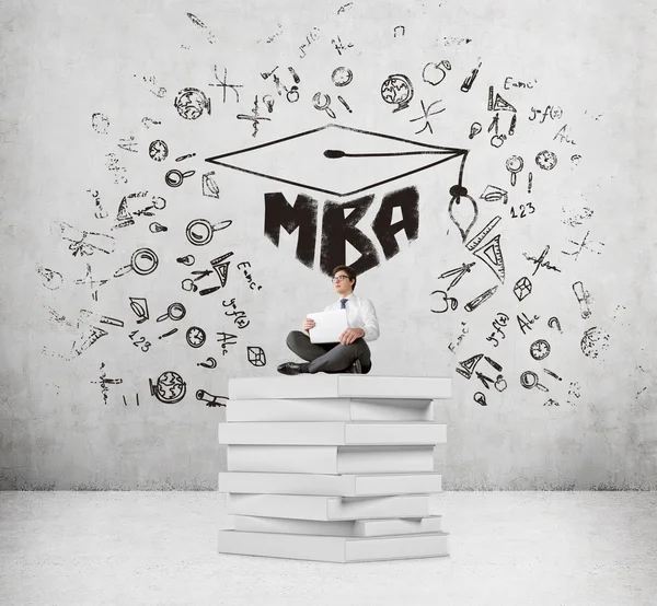 Businessman with laptop sitting on pile of books, MBA and science icons around. Concrete background. Concept of studying. — Stock Photo, Image