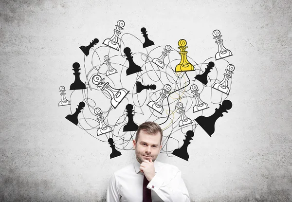Homme d'affaires avec la main sur le menton, figures d'échecs dessinées sur un mur de béton derrière, pion jaune. Concept de jeu . — Photo