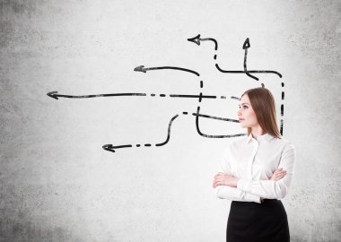 Elleri çapraz olan genç bir iş kadını elinde oklarla beton duvarın önünde duruyor..