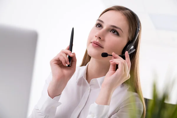 Businesswoman in headphones with microphone, pen in hand. Side view. Office. — Stock Photo, Image