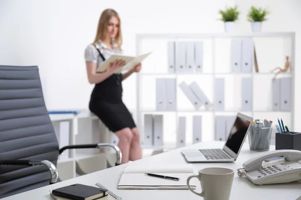 Office table, blurred blonde businesswoman standing at table at background. Office. Concept of work. — Stock Photo, Image