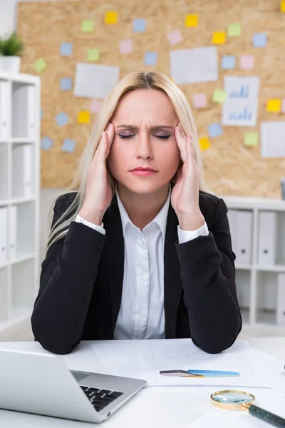 Businesswoman with hands to temples in front of computer. — Stock Photo, Image