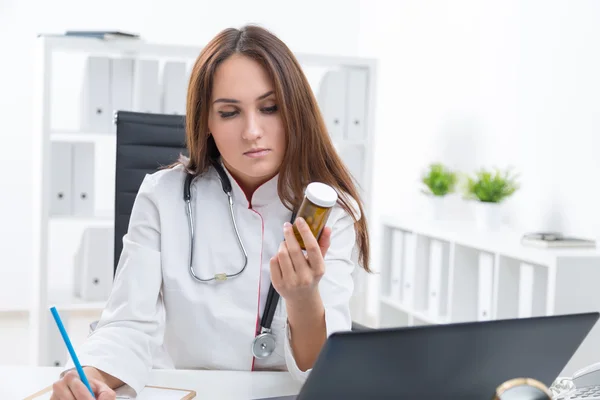 Médica trabalhando no computador, fazendo anotações e olhando para pílulas . — Fotografia de Stock