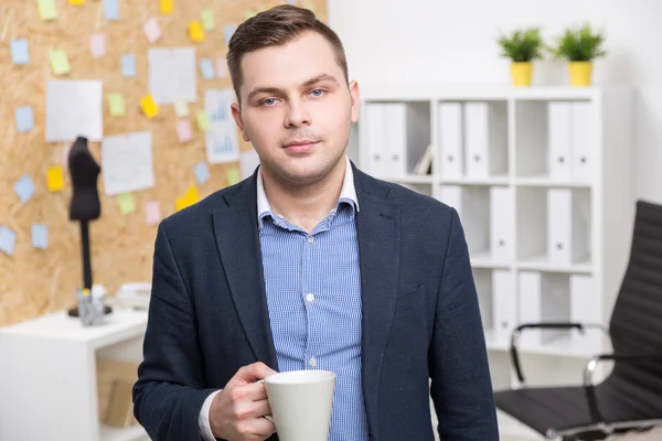 Biznesmen z białym kubka stoi. Widok z przodu. Biuro w tle. Koncepcja pracy. — Zdjęcie stockowe