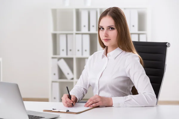 Empresaria sentada frente al portátil y tomando notas, mirando al frente . — Foto de Stock