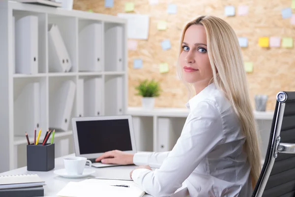 Blonde businesswoman in front of laptop, hand on keyboard. Side view. — Stock Photo, Image