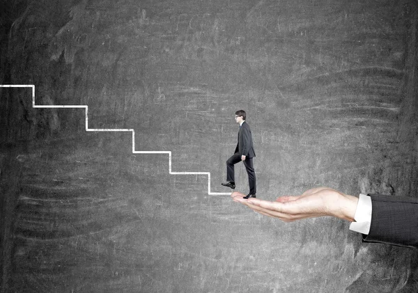 Hand holding zakenman beginnen te beklimmen trap getekend op zwarte muur. — Stockfoto