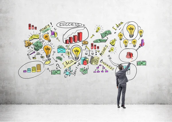 Joven empresario dibujando iconos de negocios de colores en la pared de hormigón . — Foto de Stock