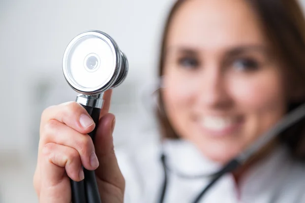 Médica sorrindo segurando fonendoscópio, olhar embaçado. Conceito de ajuda médica . — Fotografia de Stock