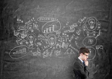 Genç işadamı çene ayakta iş ikonları/simgeleri ile siyah duvar önünde el ile. Yan görünümü. İş kurma kavramı.