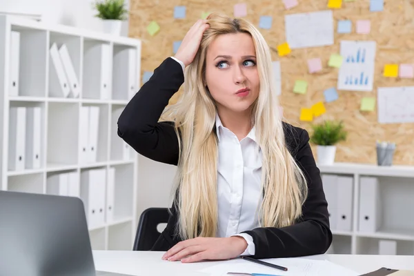Affärskvinna med hand i håret framför datorn, förbryllad utseende. Kontor i bakgrunden. Begreppet arbete. — Stockfoto