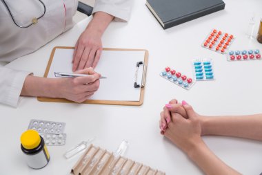 Doktor hastayı dinliyor ve notlar alıyor. Sadece eller görüldü. Masada haplar var. Tıbbi konsültasyon kavramı.