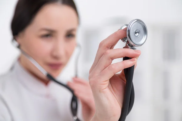 Hand with stethoscope, blurred doctor's face at background. Close up. Side view. Concept of medical examination.