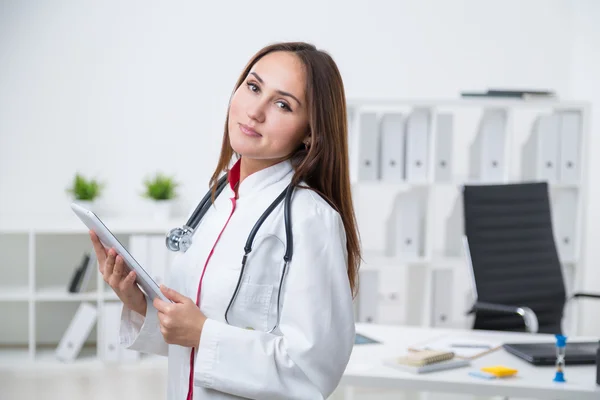 Doctora de pie en la mesa y sosteniendo el comprimido. Oficina en segundo plano. Concepto de trabajo . —  Fotos de Stock