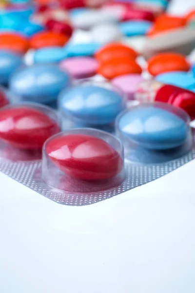 Packung mit roten und blauen Pillen, viele farbige Pillen unterschiedlicher Größe im Hintergrund. Nahaufnahme. Konzept der Medizin. — Stockfoto