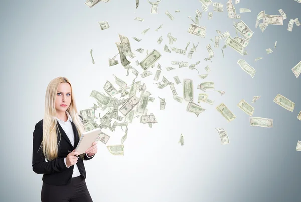 Joven mujer de negocios con cuaderno, dólares volando de él. Fondo gris. Concepto de hacer dinero . — Foto de Stock