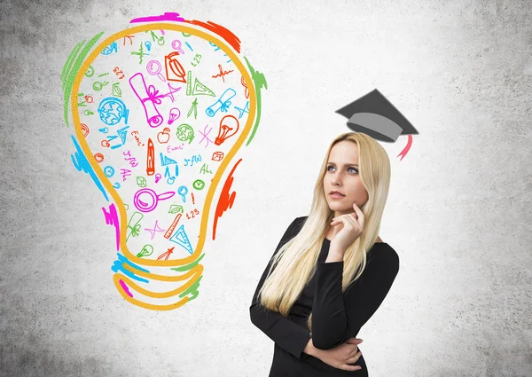 İş kadını eliyle yanakta, akademik şapkasını üzerine çizilmiş, soldaki renkli ampul. Beton arka plan. Eğitim kavramı. — Stok fotoğraf