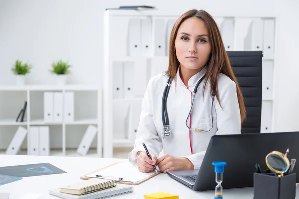 Une femme médecin assise à table. Bureau à l'arrière-plan. Concept de travail . — Photo
