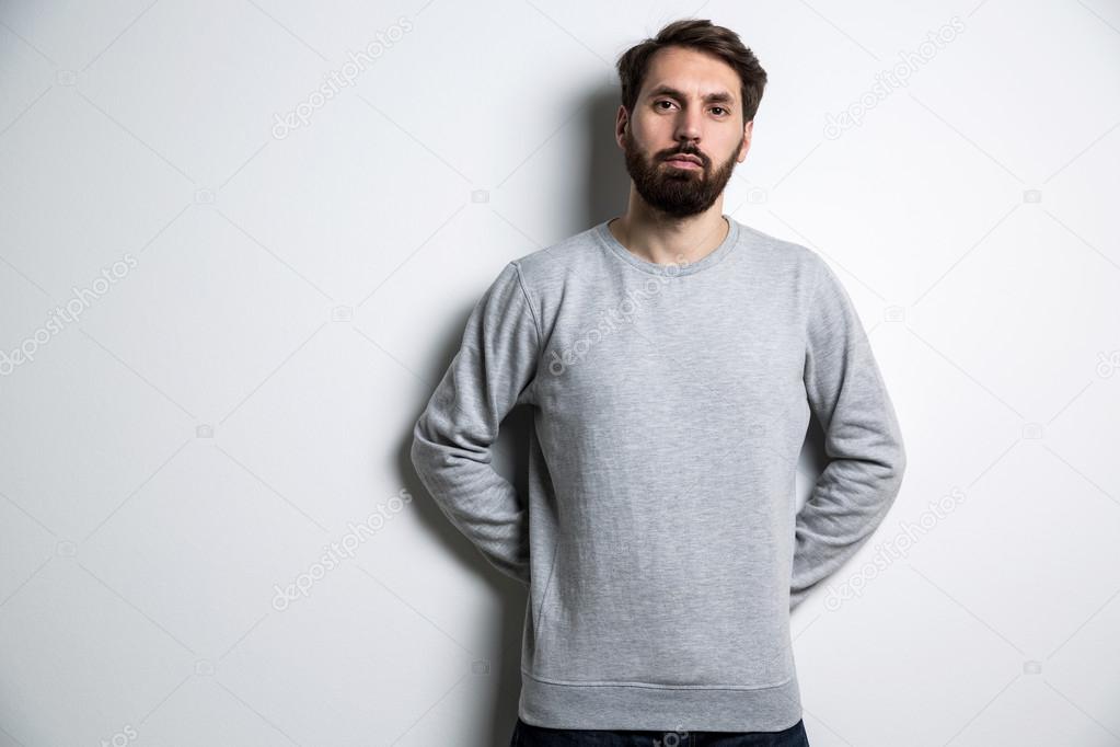 Young bearded man in grey shirt with long sleeves on light grey background. Mock up