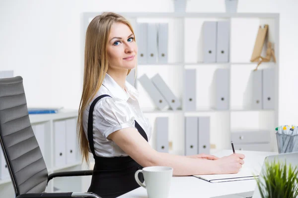 Attractive caucasian businesswoman sitting at office desk and writing — Stock Photo, Image