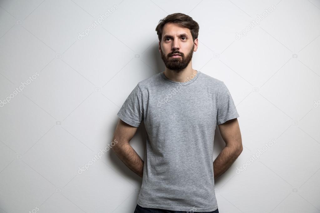 Young man dressed in blank grey shirt on light background. Mock up