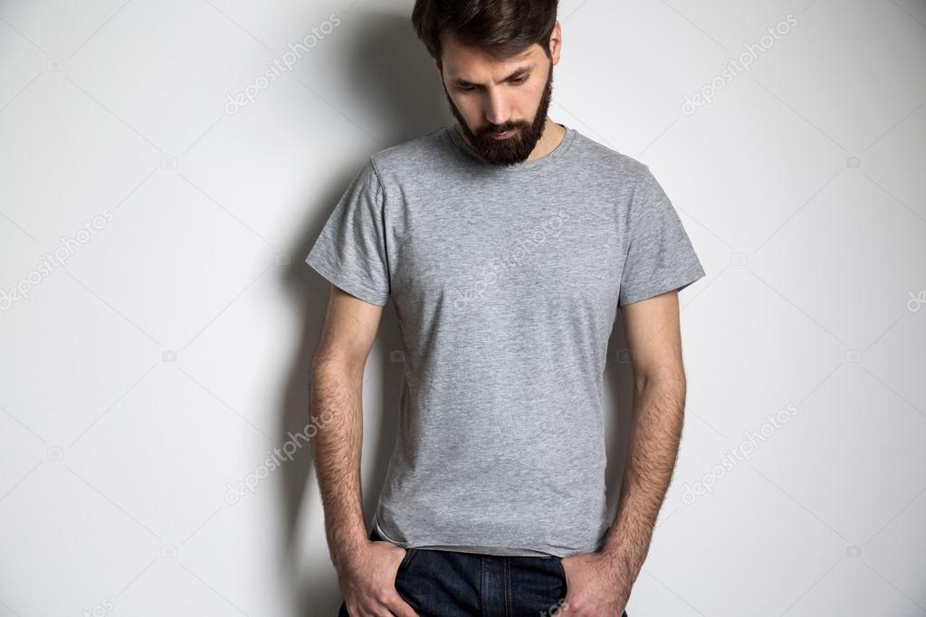 Bearded man in grey shirt with short sleeves looking down on grey background. Mock up