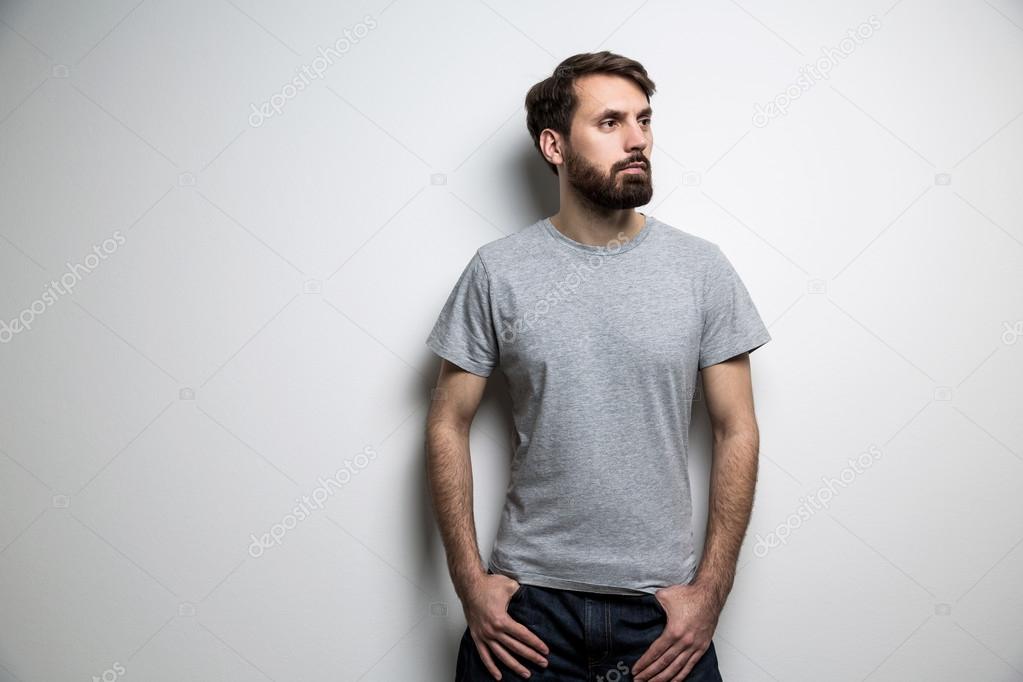Caucasian man with beard dressed in grey t-shirt on light background. Mock up