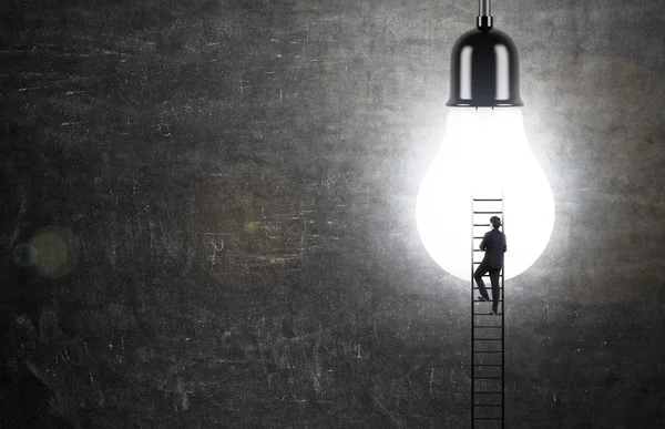 Idea concept with businessman climbing ladder to illuminated lightbulb on chalkboard background — Stock Photo, Image