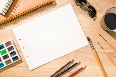 Üstten Görünüm boş kağıt sayfası, suluboya boya, kahve, Boya fırçaları, gözlük ve diğer öğeleri ile yaratıcı masaüstü. Yukarı alay