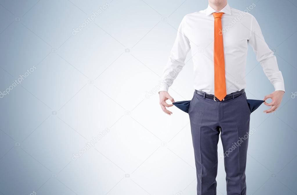 Unemployment concept with businessman showing empty pockets on grey background.