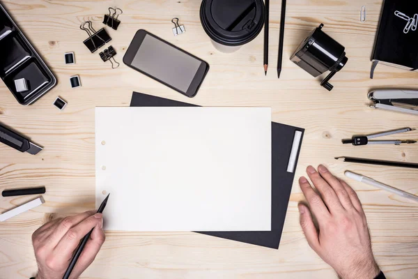 Vista dall'alto del desktop in legno con mani che disegnano su foglio di carta bianco, smartphone e vari articoli di cancelleria. Scherzi? — Foto Stock