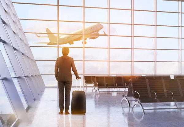 Concepto de viaje con hombre de negocios y una maleta en el interior del aeropuerto con avión volando. Renderizado 3D —  Fotos de Stock