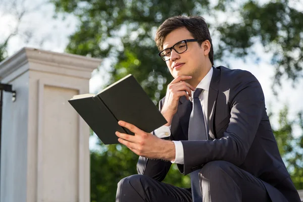 Мыслящий бизнесмен читает книгу снаружи — стоковое фото