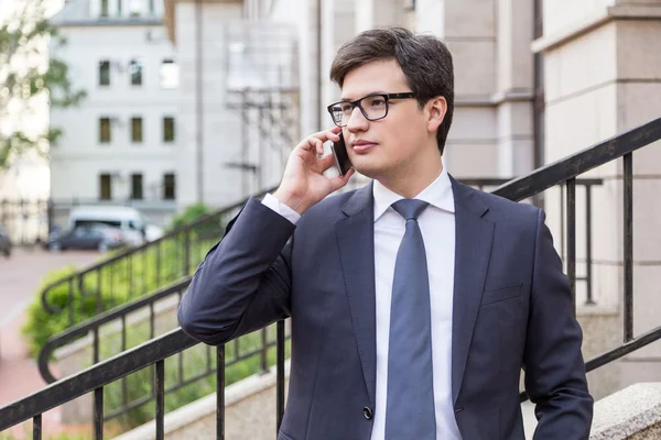 Un joven hombre de negocios de traje hablando por teléfono. Edificio de baldosas de hormigón en el fondo — Foto de Stock