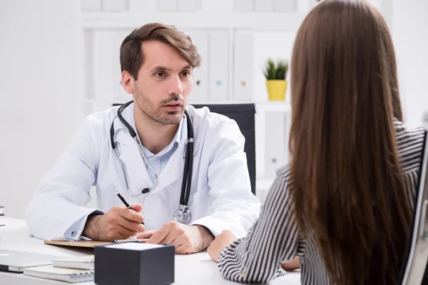 El doctor está escuchando a su paciente hablar de los síntomas sentados en la silla de su oficina. Concepto de toma de decisiones médicas . — Foto de Stock