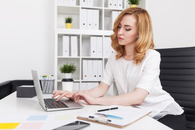 Büyük şehir odasında dizüstü bilgisayarında yazan bir kadın. Pano ve ofis malzemeleri masanın üzerinde. Sekreterlik işi kavramı. 