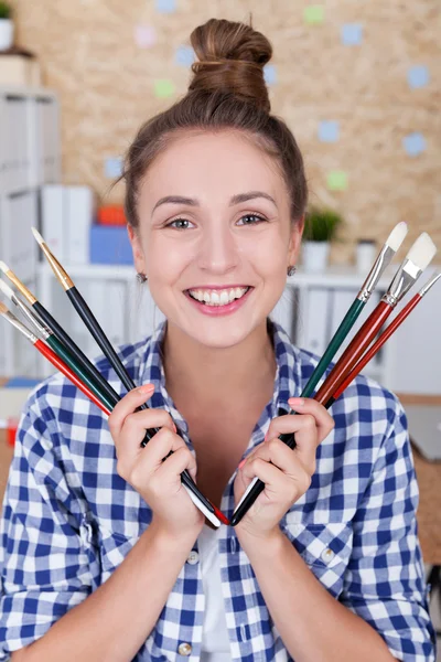 Donna sorridente in camicia a scacchi blu sta tenendo mazzo di pennelli in entrambe le mani. Concetto di creazione e arte . — Foto Stock