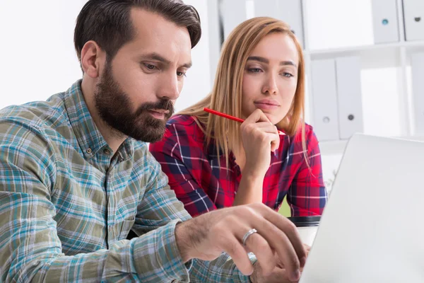 Dois designers trabalhando juntos no escritório e olhando para a tela do computador. A mulher está a segurar num lápis. O homem está a escrever. Conceito de trabalho criativo — Fotografia de Stock