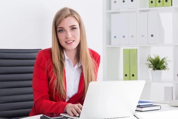 Senhora de negócios bonita em terno vermelho sentado perto de seu laptop com a mão no teclado. Conceito de gerente atraente — Fotografia de Stock