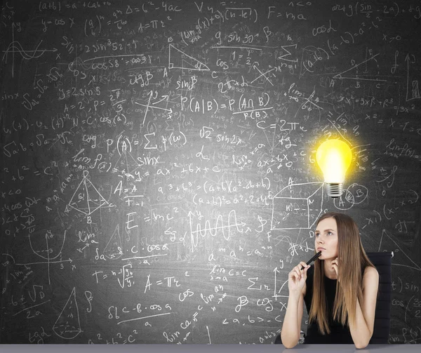 Retrato de mulher cientista sentado perto de quadro-negro com fórmulas e esboço de lâmpada acima de sua cabeça. Conceito de ideia brilhante em pesquisa — Fotografia de Stock