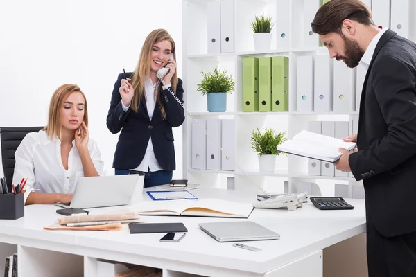 La femme d'affaires parle au téléphone. Son collègue regarde l'écran de l'ordinateur portable légèrement ennuyé. Leur collègue masculin lit un livre. Concept de routine d'entreprise — Photo