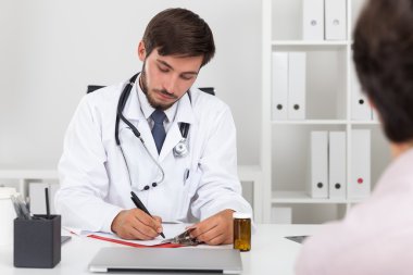 Concentrated doctor with beard in white goan writing down patient's symptoms. Concept of anamnesis gathering clipart