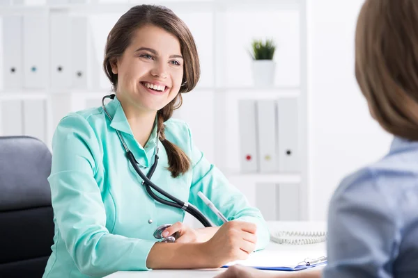 Молода жінка-лікар розмовляє зі своїм пацієнтом. Вона дійсно задоволена результатами лікування і посміхається широко — стокове фото