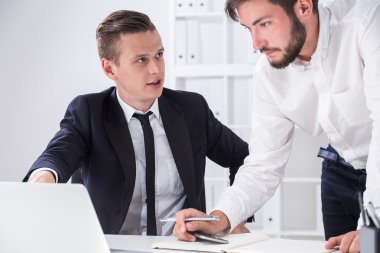 Bir meslektaşım dizüstü bilgisayar ekranını işaret ediyor ve ortağının çalışmalarının sonuçlarını gösteriyor. İş yerinde işbirliği kavramı