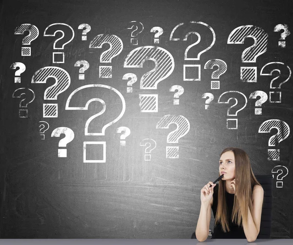 Sitting girl and question marks on blackboard