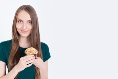 Yeşil tişörtlü ince kız kek tutuyor ve gülümsüyor. Sağlıklı beslenme alışkanlıkları ve suçlu zevkleri kavramı. Alay etmek