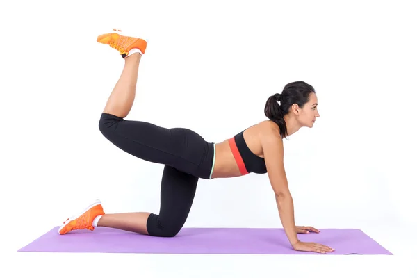 Die schlanke Sportlerin in schwarzer Sportkleidung trainiert auf einer violetten Matte. Konzept des Trainings und der Fitness. — Stockfoto